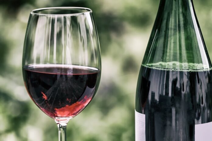 Weinglas neben Rotweinflasche im Fokus.
