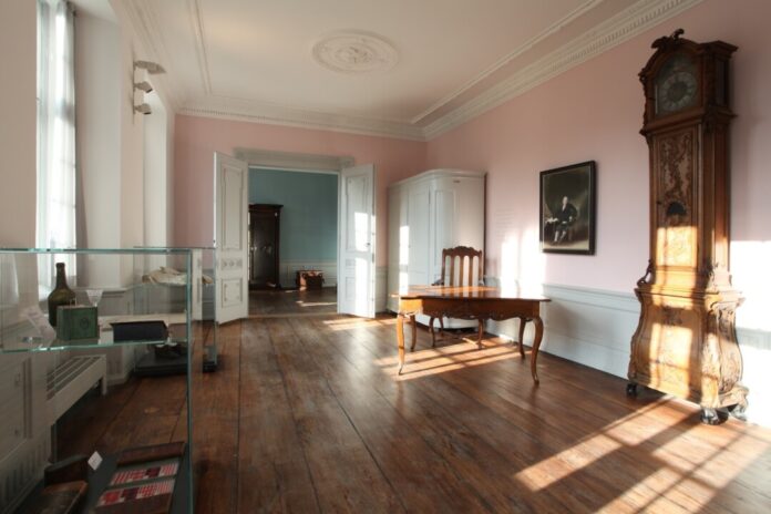 Historisches Zimmer mit Standuhr und Holztisch.