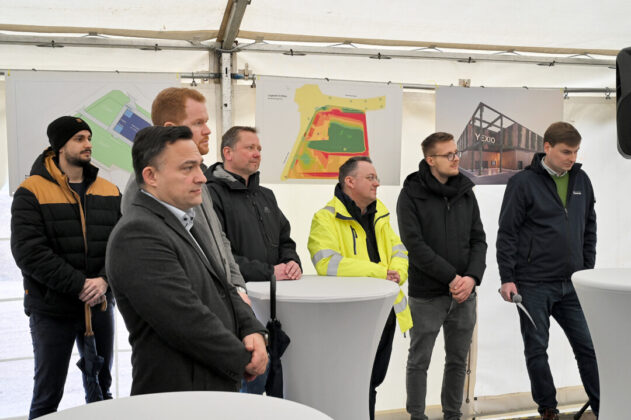 Männer bei Projektbesprechung mit Plänen im Hintergrund.
