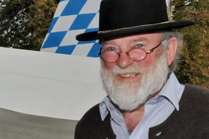 Älterer Mann mit Hut und Brille lächelt.