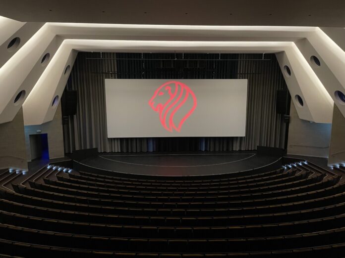 Leerer Kinosaal mit rotem Löwenlogo auf Leinwand.