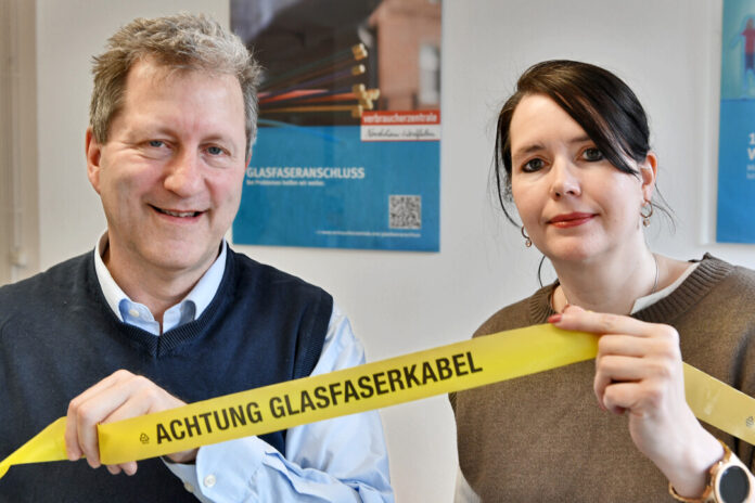 Zwei Personen halten Warnband „Achtung Glasfaserkabel“.
