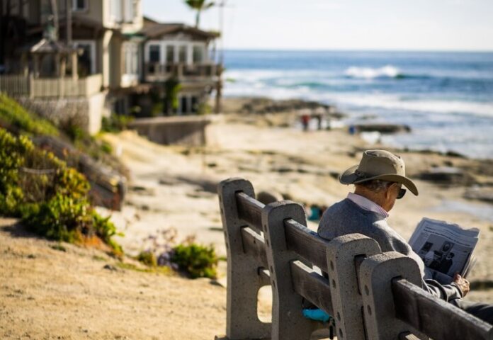 Ein älterer Mann sitzt auf einer Bank am Strand. Foto: pixabay