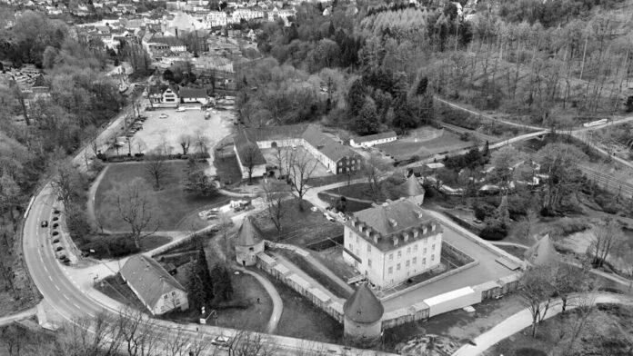 Die Ansicht zeigt das Herrenhaus mit dem Mühlengebäude (links) im Vordergrund, daran schließt sich die Vorburg in ihrer typischen U-Form an, weiter hinten der Schlossparkplatz und die Altstadt, wo das markante Dach des Mariendoms zu erkennen ist. Foto: Mathias Kehren
