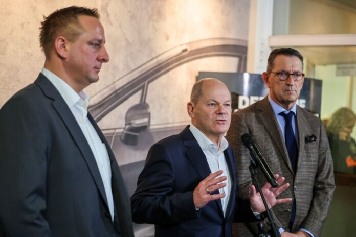 Betriebsratschef Benjamin Gruschka (l) neben Bundeskanzler Olaf Scholz (SPD) und Marcus Wassenberg (r), Geschäftsführer der Ford-Werke.
