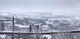 Spaziergänger gehen eine Brücke neben der Winterberger Bobbahn mit Blick auf die Landschaft im Schnee.