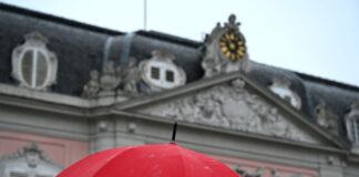 Eine Frau geht mit ihrem Regenschirm bei Regen am Schloss Benrath vorbei.