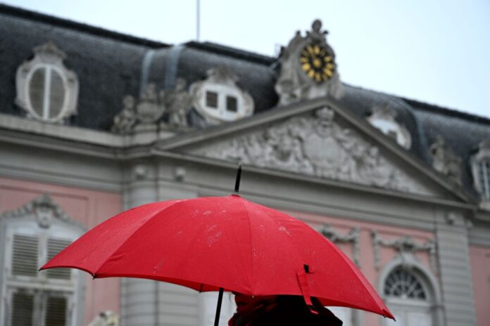 Eine Frau geht mit ihrem Regenschirm bei Regen am Schloss Benrath vorbei.