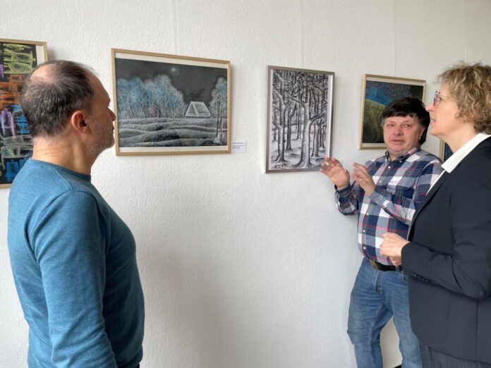 Bürgermeisterin Sandra Pietschmann, Michalis Papadopoulos (l.) und Orest Smishko, ein Freund der Künstler, schauen sich Bilder von Alexander Bondartschuk an. Foto: Kreisstadt Mettmann