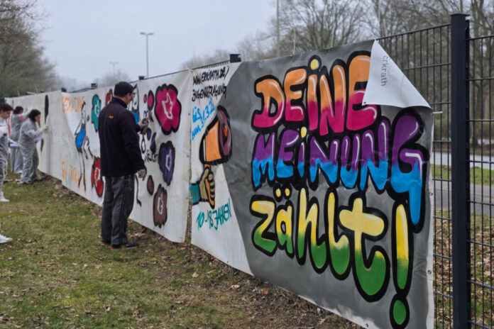 Um möglichst viele junge Menschen anzusprechen, wurde auf dem Gelände der Carl-Fuhlrott-Schule in Hochdahl eine Graffiti-Aktion mit dem Künstlerduo Tran Nguyen und Imke Hofmann durchgeführt. Auf mehreren Bauzaunbannern konnten Jugendliche ihre eigenen künstlerischen Motive gestalten und damit zur Teilnahme an der Befragung aufzurufen. Foto: Stadt Erkrath