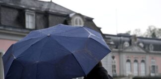 Ein Mann und eine Frau blicken beim Regenwetter auf das Schloss Benrath.