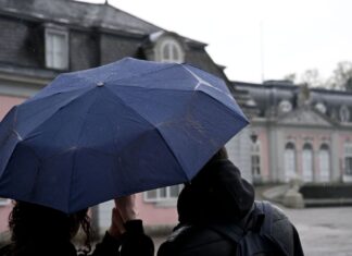 Ein Mann und eine Frau blicken beim Regenwetter auf das Schloss Benrath.
