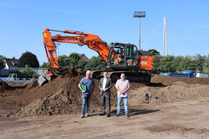 Dieser Erdhügel war mal der Stadionrasen, jedenfalls ein Teil davon, denn größtenteils war die Rasentragschicht bereits abtransportiert worden. Fachplaner Georg Schlate, Sportdezernent Patrick Anders und Projektleiter Achim Kramer (v.l.n.r.) erläuterten an Ort und Stelle die Baumaßnahme zur Erneuerung des Stadionrasens. Foto: Stadt Ratingen