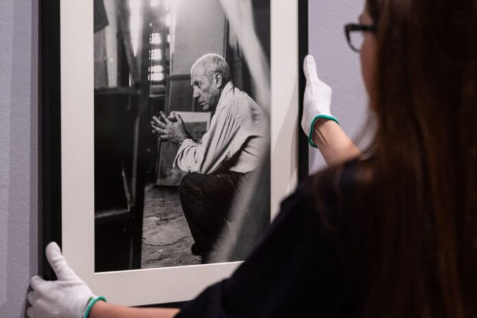 Eine Mitarbeiterin hängt ein eingerahmtes Foto von Pablo Picasso des Fotografen Herbert List an die Wand.