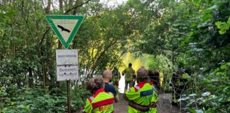 Rettungskräfte stehen an einem Seeufer unter Warnschildern. (Archivfoto)