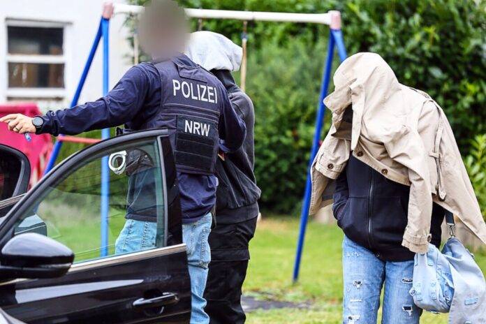 SEK-Einsatz in Herdecke Ein Polizist führt zwei Personen in Herdecke, die ihre Gesichter verdecken, zu einem Auto.