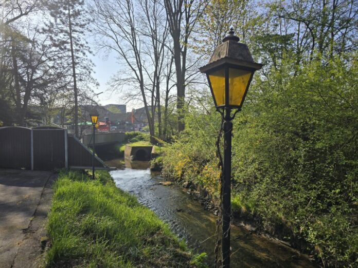 Der Dickelsbach nachdem er das Mühlengelände (im Hintergrund zu sehen) verlassen hat und am Bürgershaus vorbe seinen Weg durch das schöne Lintorf fortsetzt. Bild: Alexander Heinz