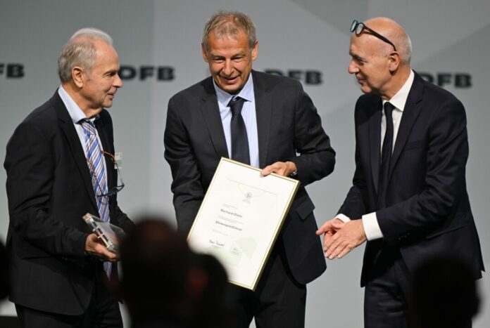45. DFB-Bundestag in Frankfurt am Main Bernard Dietz (l) wird von Jürgen Klinsmann und DFB-Präsident Bernd Neuendorf für die Ernennung zum Ehrenspielführer gratuliert.