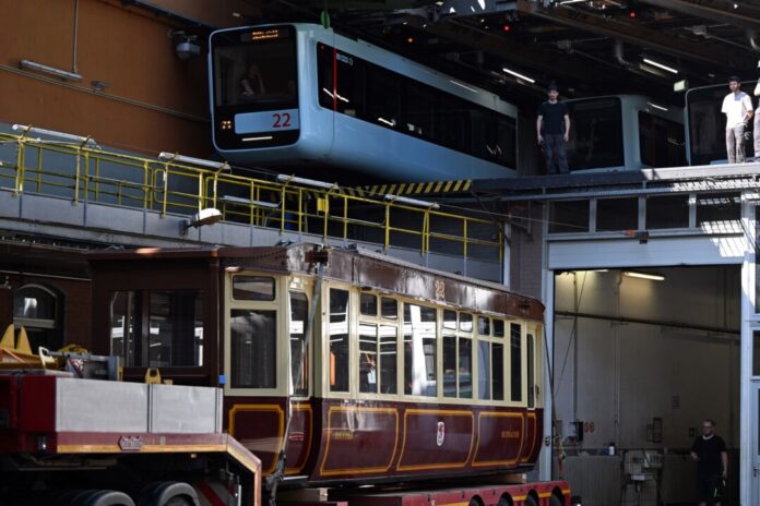 Die Schwebebahn gestern und heute. Ein Wagen der ersten Baureihe 1900 steht auf einem Tieflader unter einem Wagen der aktuellen Baureihe in der Werkstatt der Schwebebahn. (Archivbild)