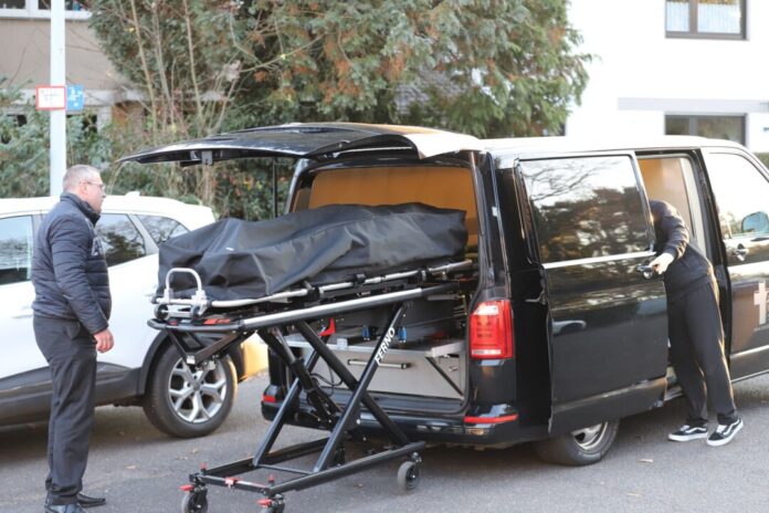 Frau fällt in Teich und ertrinkt Bestatter laden eine Leiche in einen Leichenwagen.