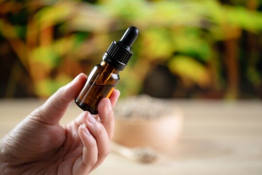 Hands holding a bottle of legalized CBD oil and its dropper lid with hemp leaf. „100 % vegan“, „laktosefrei“ oder „glutenfrei“ sind in diesem Fall keine Qualitätskriterien, sondern verschleiern die Gefahr, Bild: VZ NRW