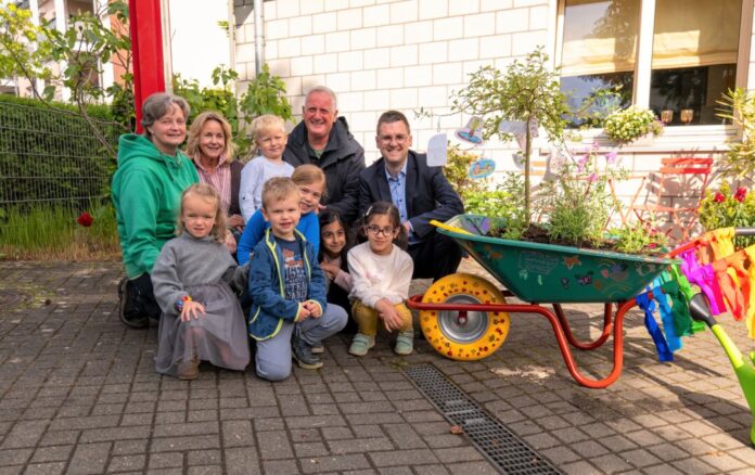 2026-05-15 KiTa_bepflanzte Schubkarren Final Kinder der Kita an der Krummenweger Straße und ihre Einrichtungsleiterin Claudia Weber (2.v.l.) erläuterten Bürgermeister Patrick Anders (rechts) gern, wie sie die Schubkarre gestaltet und bepflanzt haben. Mit dabei waren Ursula Merlo und Heribert Müller vom städtischen Grünflächenamt. Foto: Stadt Ratingen