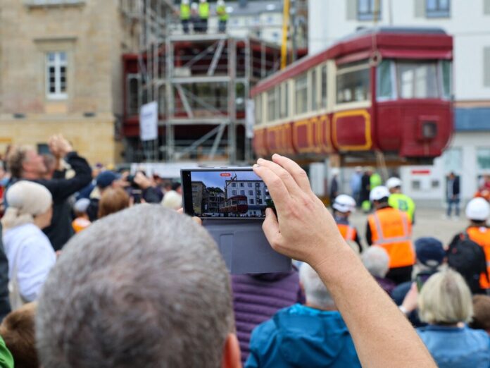 Schwebebahnwagen wird in den Hauptbahnhof gehoben Hunderte Schaulustige verfolgen die Platzierung des Schwebebahnwagens auf einer Stahlkonstruktion zwischen zwei Gebäude.