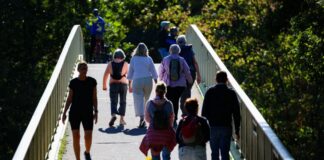 Sommerliche Temperaturen in NRW Spaziergänger laufen bei Sonnenschein über eine Brücke.