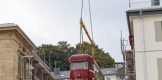 Eine Schwebebahn kehrt heim und wird zum Blickfang Ein historischer Schwebebahnwagen wird von einem Tieflader auf eine Stahlkonstruktion zwischen zwei Gebäuden gehoben.
