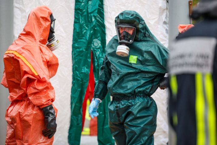 Explosion in Lagerhalle in Bochum - ein Toter Beamte in Schutzanzügen nach der Explosion in Bochum. Möglicherweise wurden dort giftige Chemikalien gelagert.