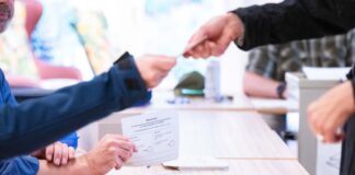 Städte erhöhen Aufwandsentschädigung für Wahlhelfer Ein Wahlhelfer übergibt einer Wählerin den Stimmzettel zur Stichwahl zur Kommunalwahl in einem Bonner Wahllokal (Archivfoto)