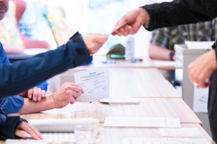 Städte erhöhen «Erfrischungsgeld» für Wahlhelfer Ein Wahlhelfer übergibt einer Wählerin den Stimmzettel zur Stichwahl zur Kommunalwahl in einem Bonner Wahllokal (Archivfoto)